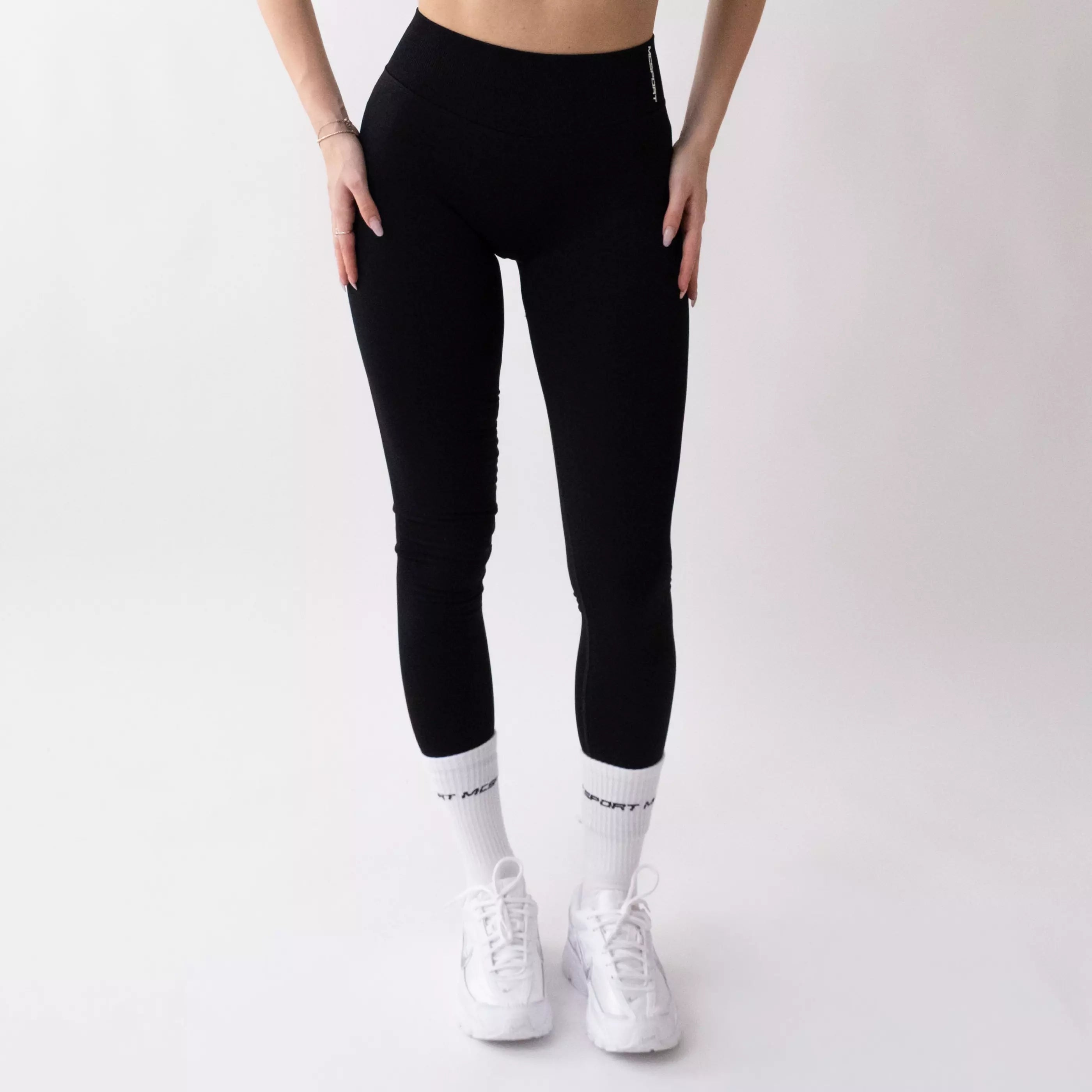Leggings sportivi neri da donna indossati con fascia alta in vita, morbidi ed elasticizzati.