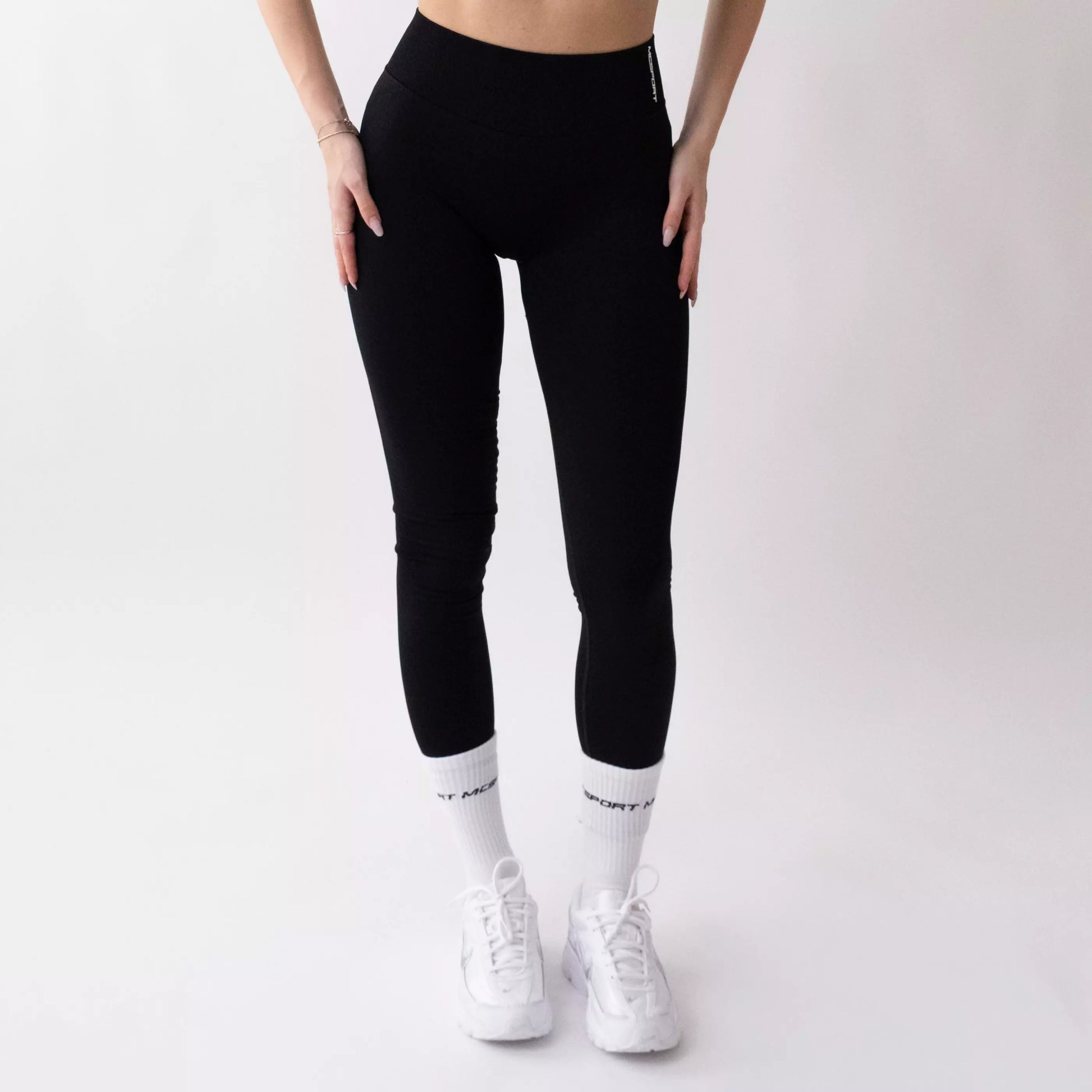 Leggings sportivi neri da donna indossati con fascia alta in vita, morbidi ed elasticizzati.