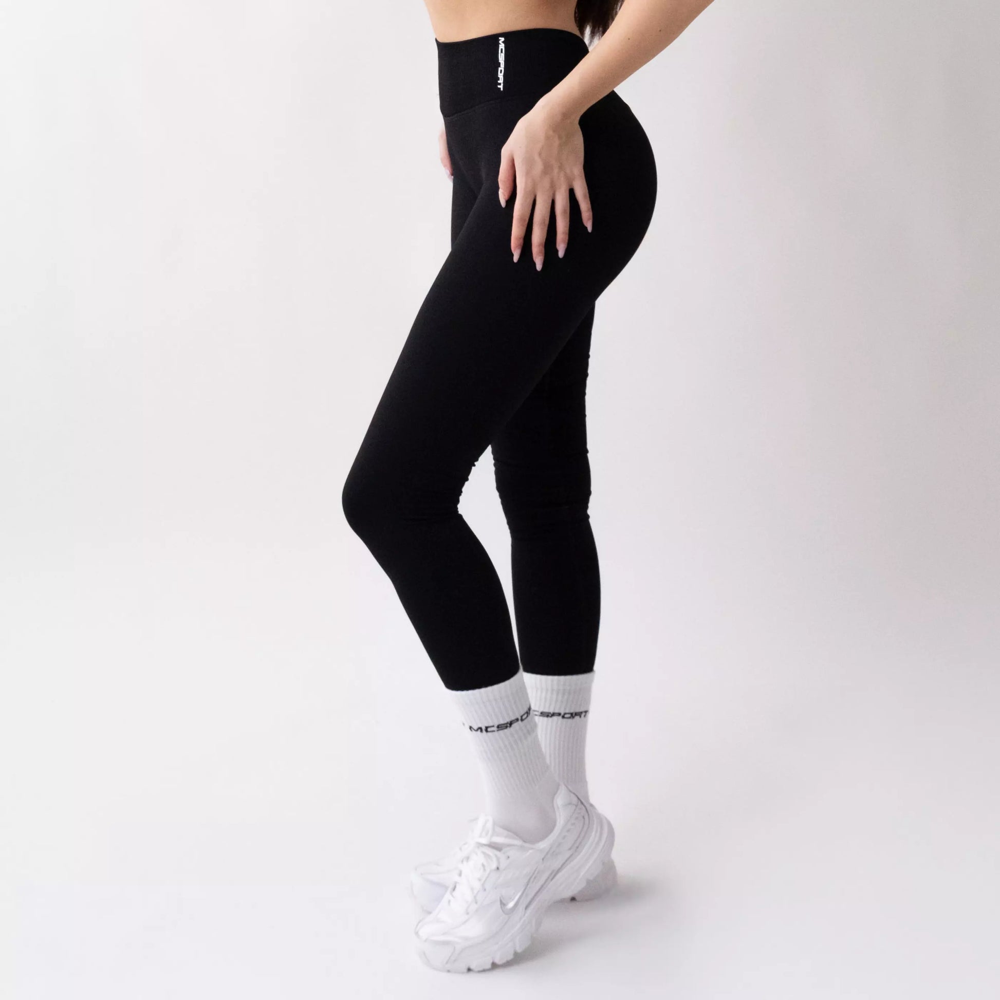 Leggings sportivi neri da donna indossati con fascia alta in vita, morbidi ed elasticizzati.