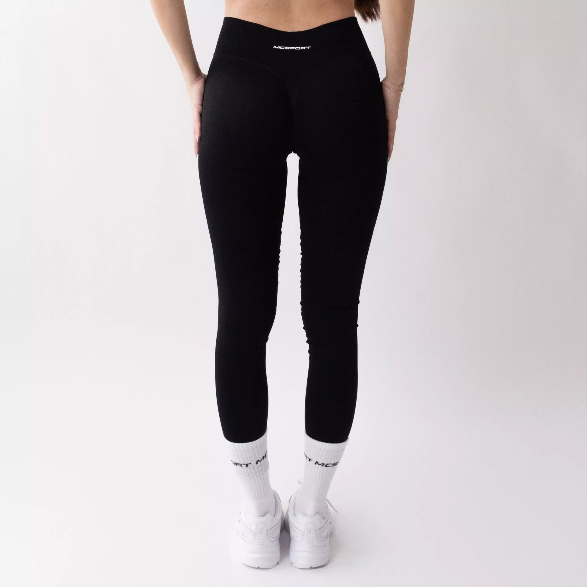 Leggings sportivi neri da donna indossati con fascia alta in vita, morbidi ed elasticizzati.