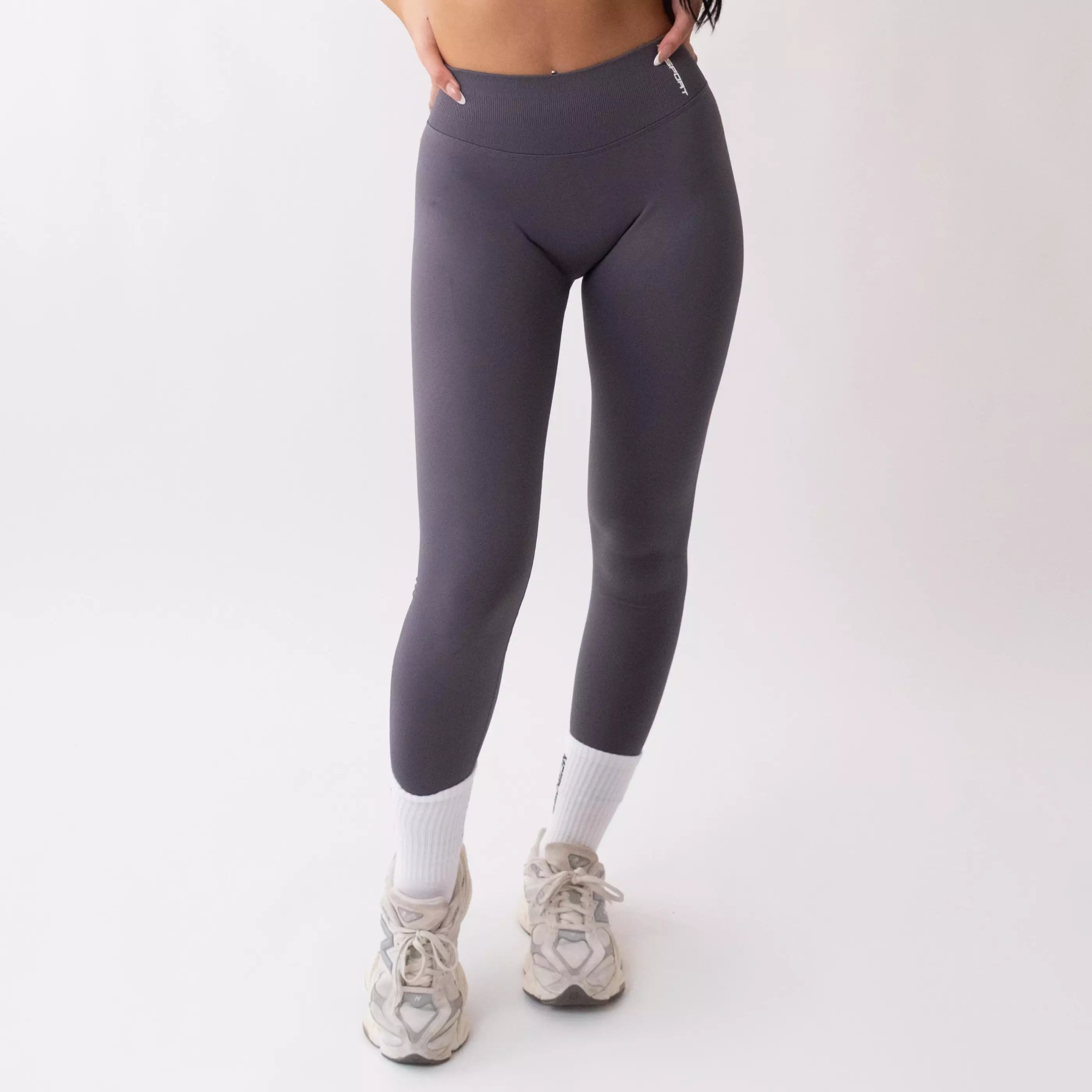 Leggings sportivi grigi da donna indossati con fascia alta in vita, morbidi ed elasticizzati.