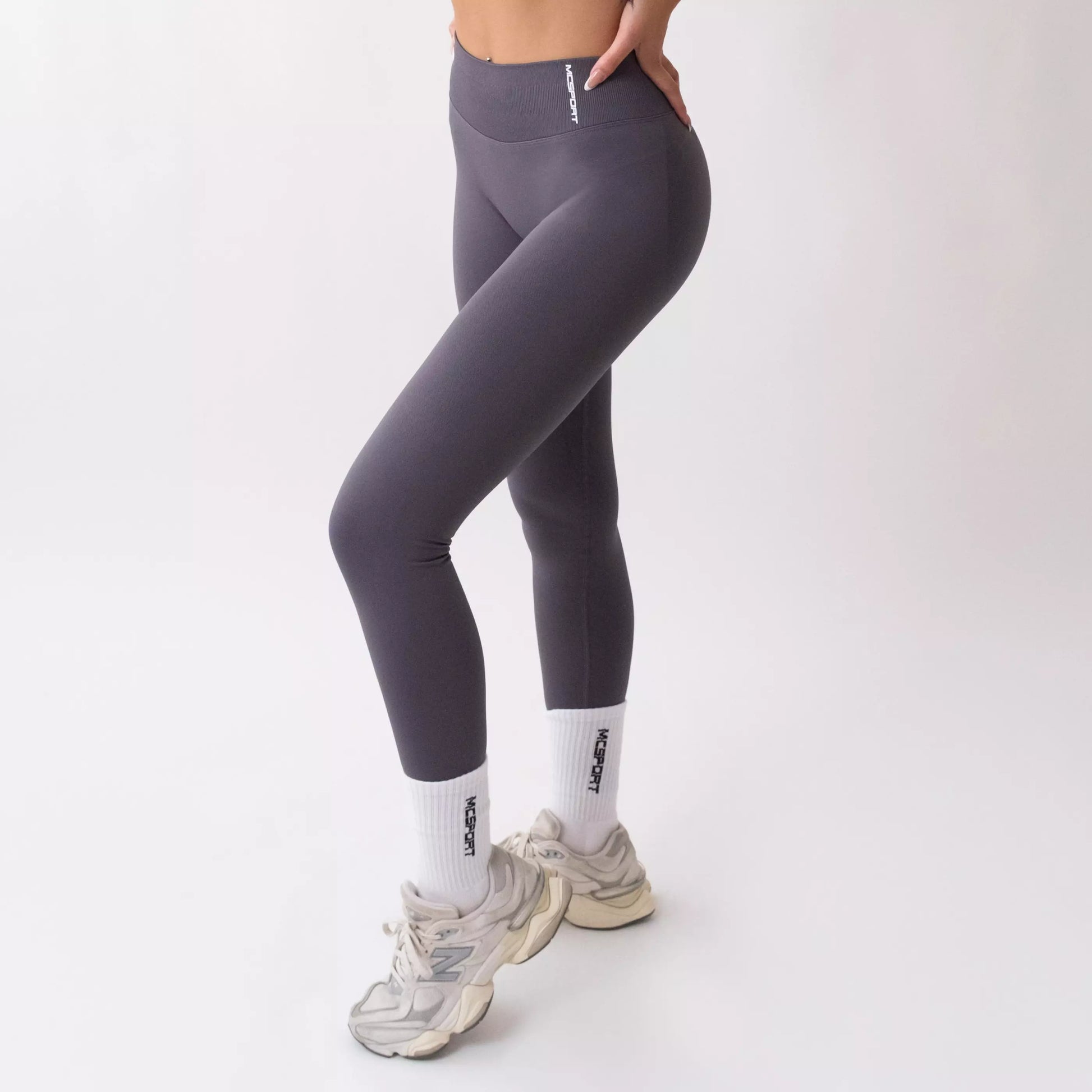 Leggings sportivi grigi da donna indossati con fascia alta in vita, morbidi ed elasticizzati.