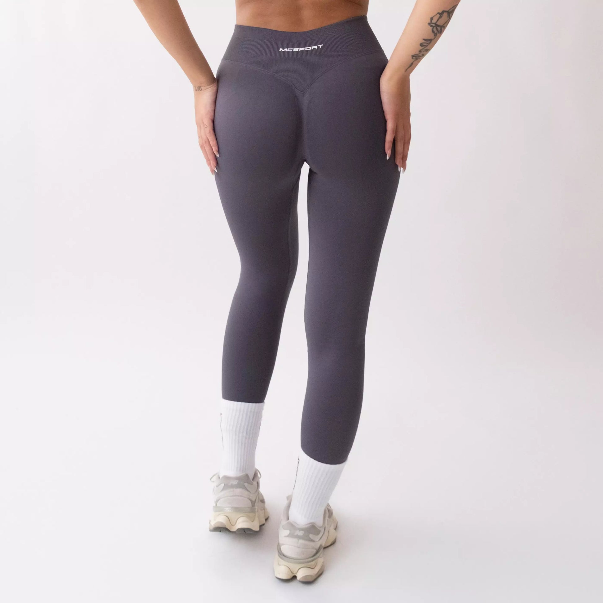 Leggings sportivi grigi da donna indossati con fascia alta in vita, morbidi ed elasticizzati.