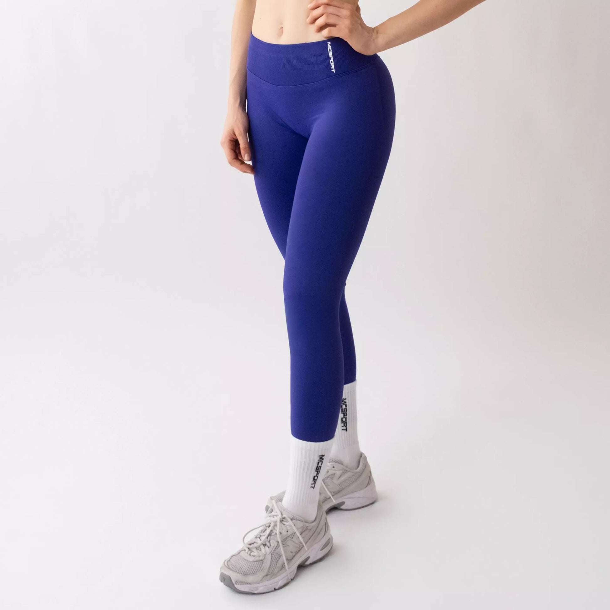 Leggings sportivi viola da donna indossati con fascia alta in vita, morbidi ed elasticizzati.