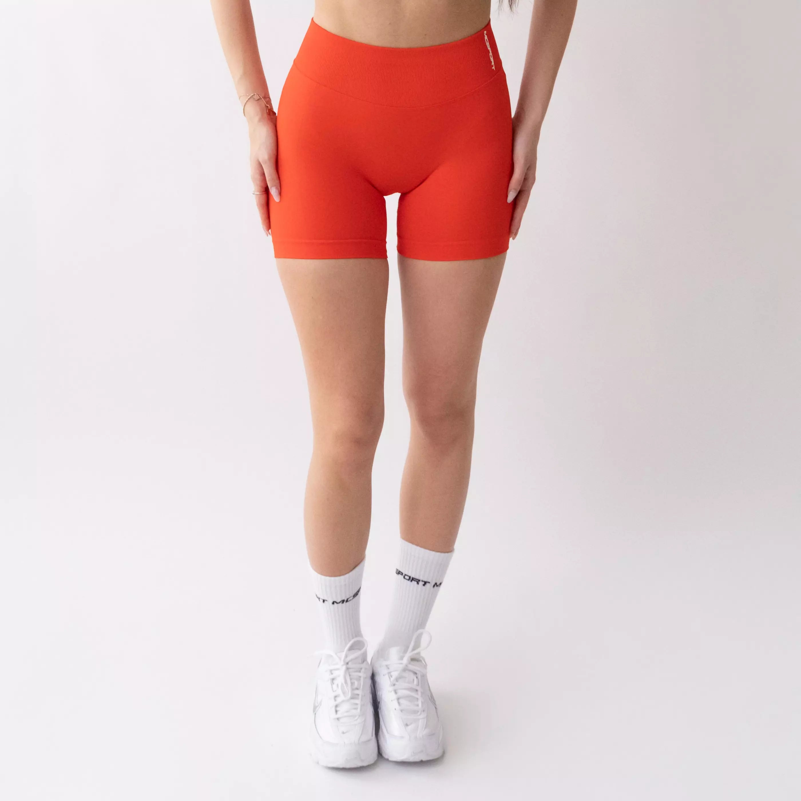 Shorts sportivi color corallo da donna indossati con fascia alta in vita, morbidi ed elasticizzati.