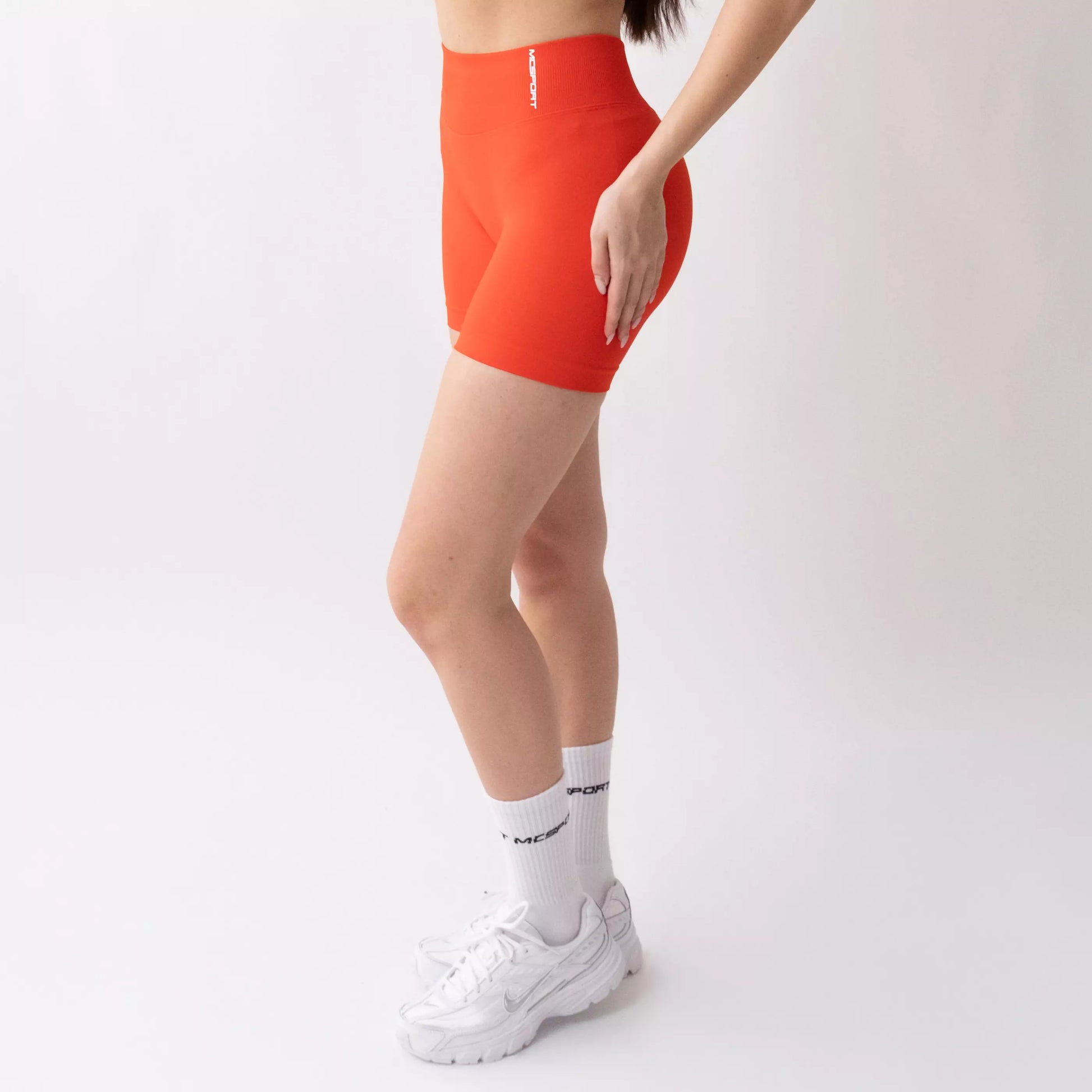 Shorts sportivi color corallo da donna indossati con fascia alta in vita, morbidi ed elasticizzati.
