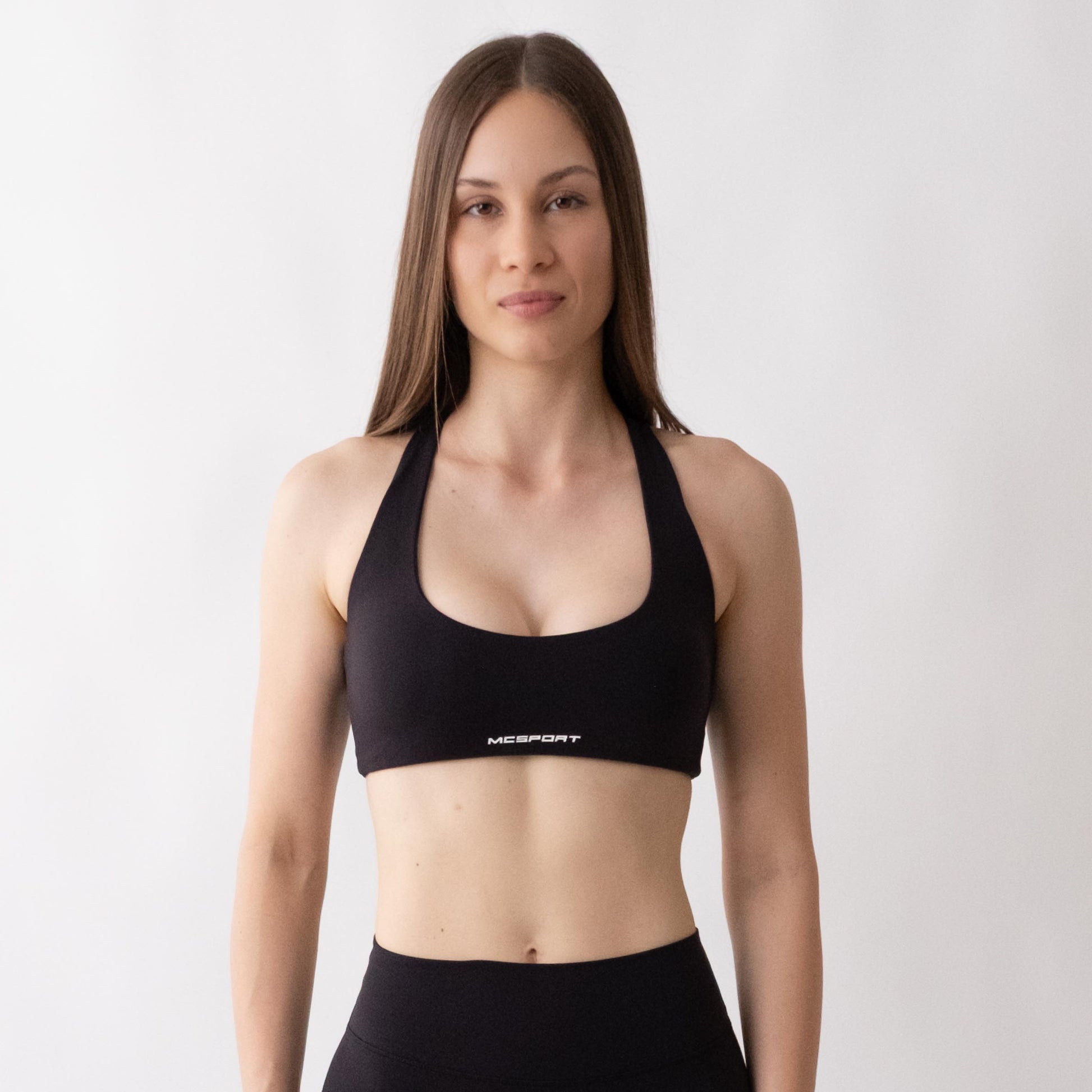 Top sportivo nero da donna indossato con schiena olimpionica: tessuto elasticizzato, supporto confortevole e libertà di movimento per fitness, yoga, pilates e allenamenti.