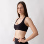 Top sportivo nero da donna indossato con schiena olimpionica: tessuto elasticizzato, supporto confortevole e libertà di movimento per fitness, yoga, pilates e allenamenti.