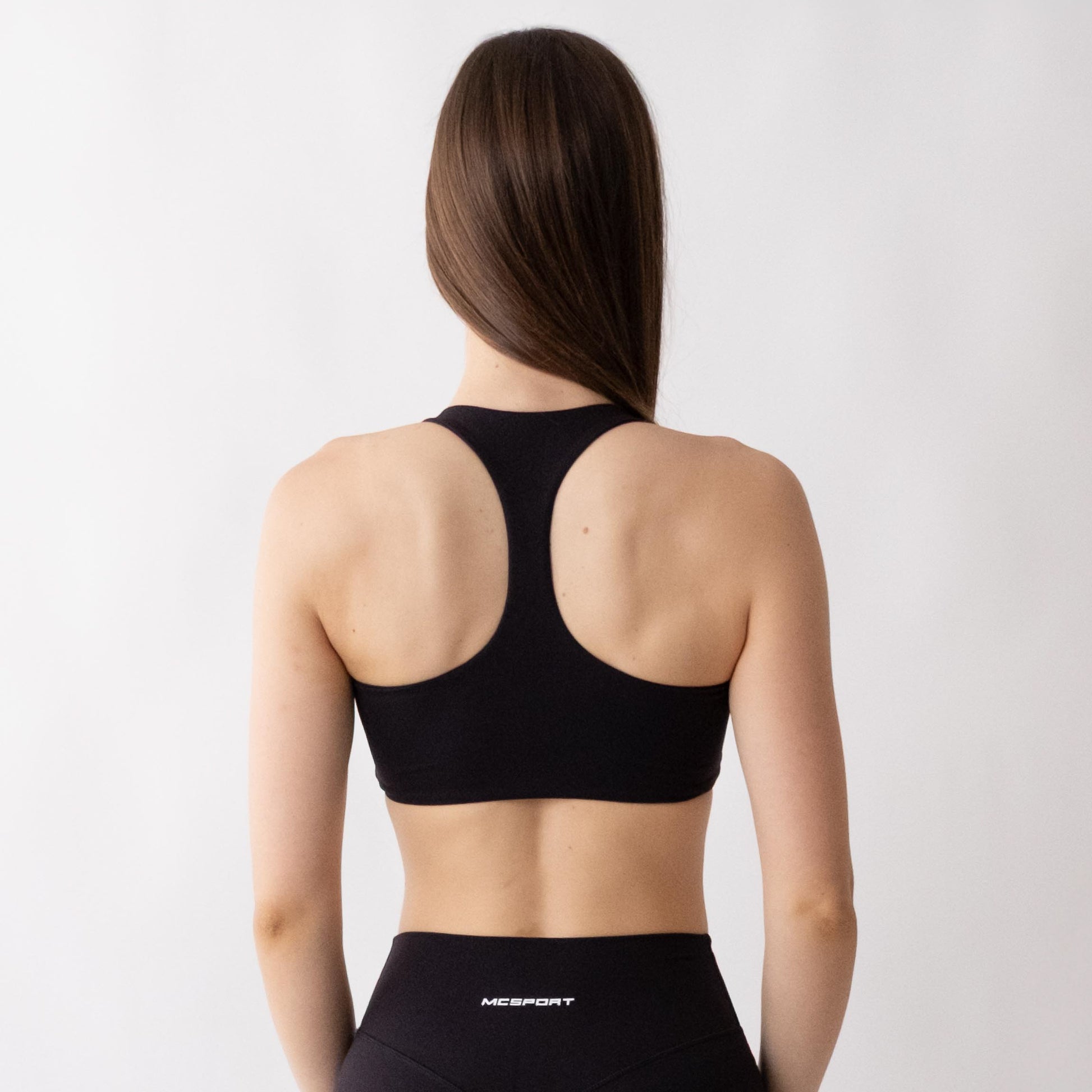 Top sportivo nero da donna indossato con schiena olimpionica: tessuto elasticizzato, supporto confortevole e libertà di movimento per fitness, yoga, pilates e allenamenti.