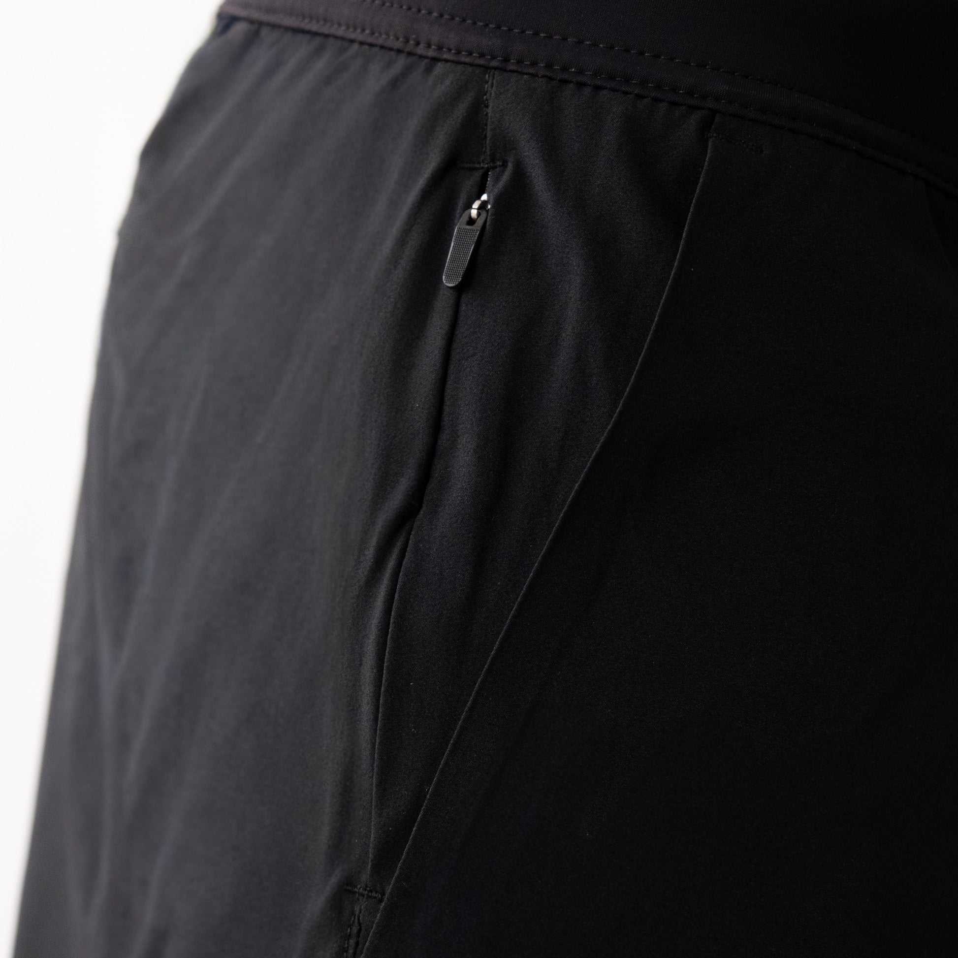 Dettaglio pantaloncini neri sportivi da uomo indossati con tessuto 4-way stretch e tasca con zip.